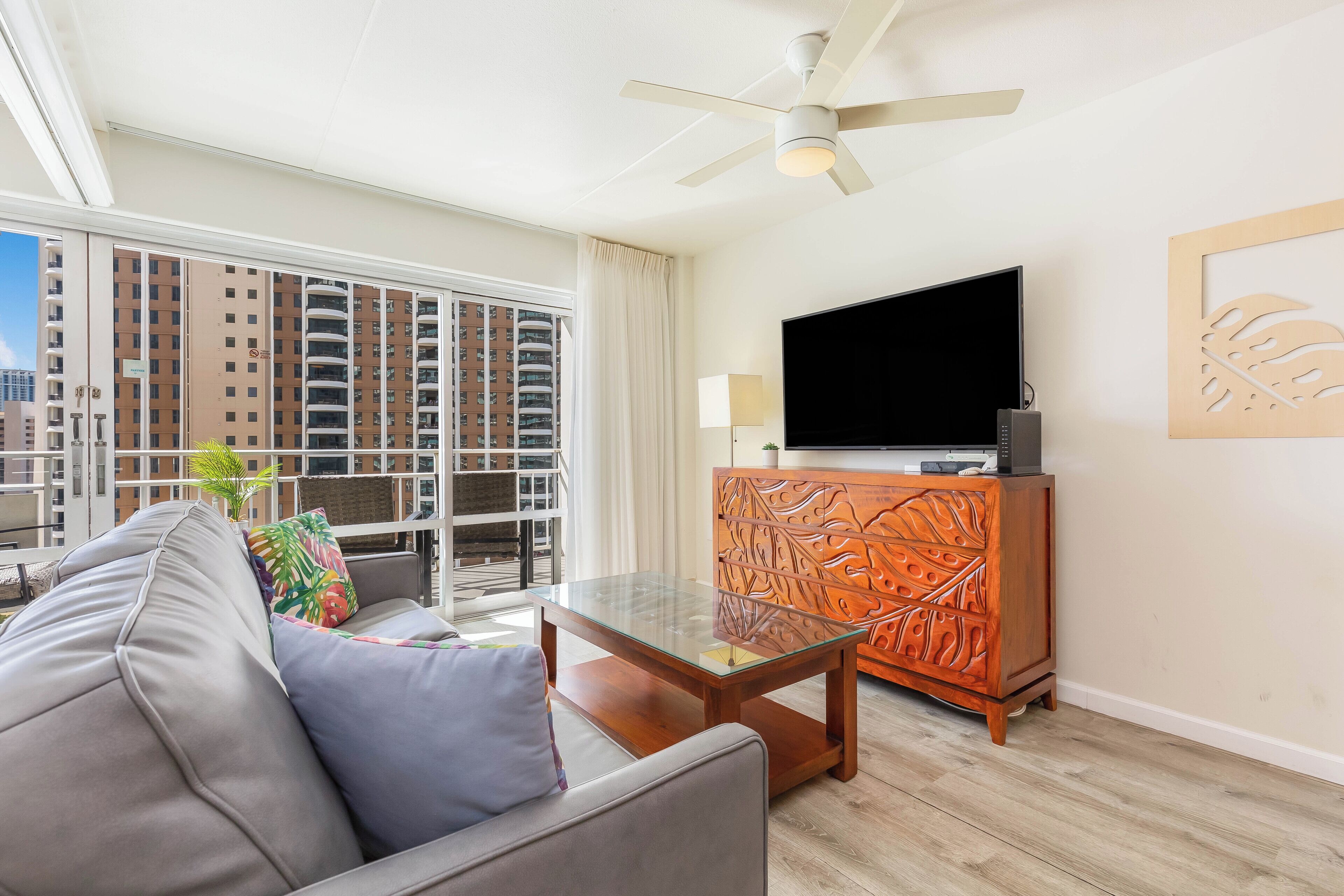 A modern living room with a sofa, a glass coffee table, a flat-screen TV, and a decorative wooden cabinet.
