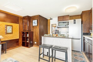 Une cuisine avec des meubles de rangement en bois, un four à micro-ondes, un réfrigérateur et deux tabourets.