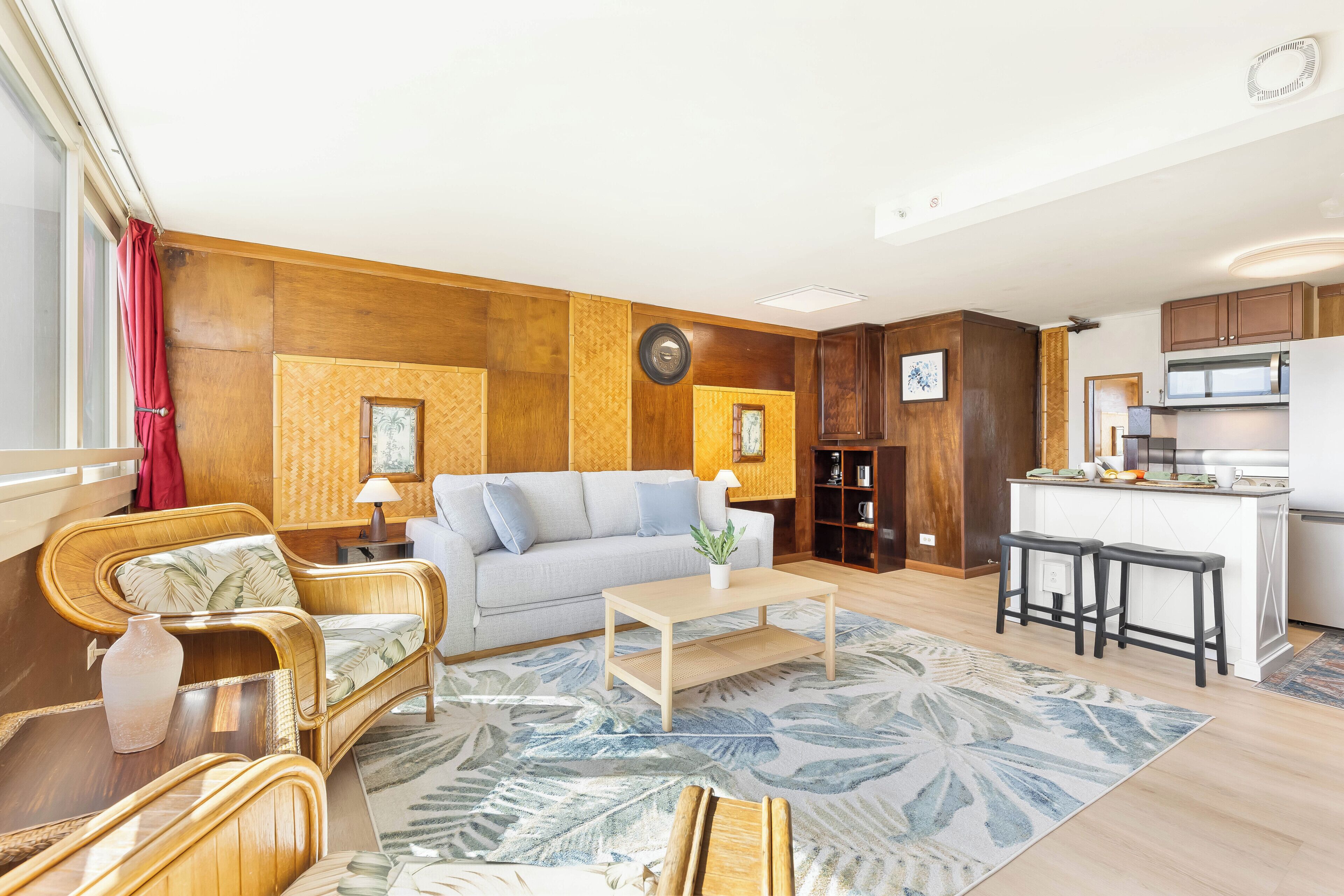 A living room with a sofa, coffee table, and a kitchen area with a microwave and bar stools.