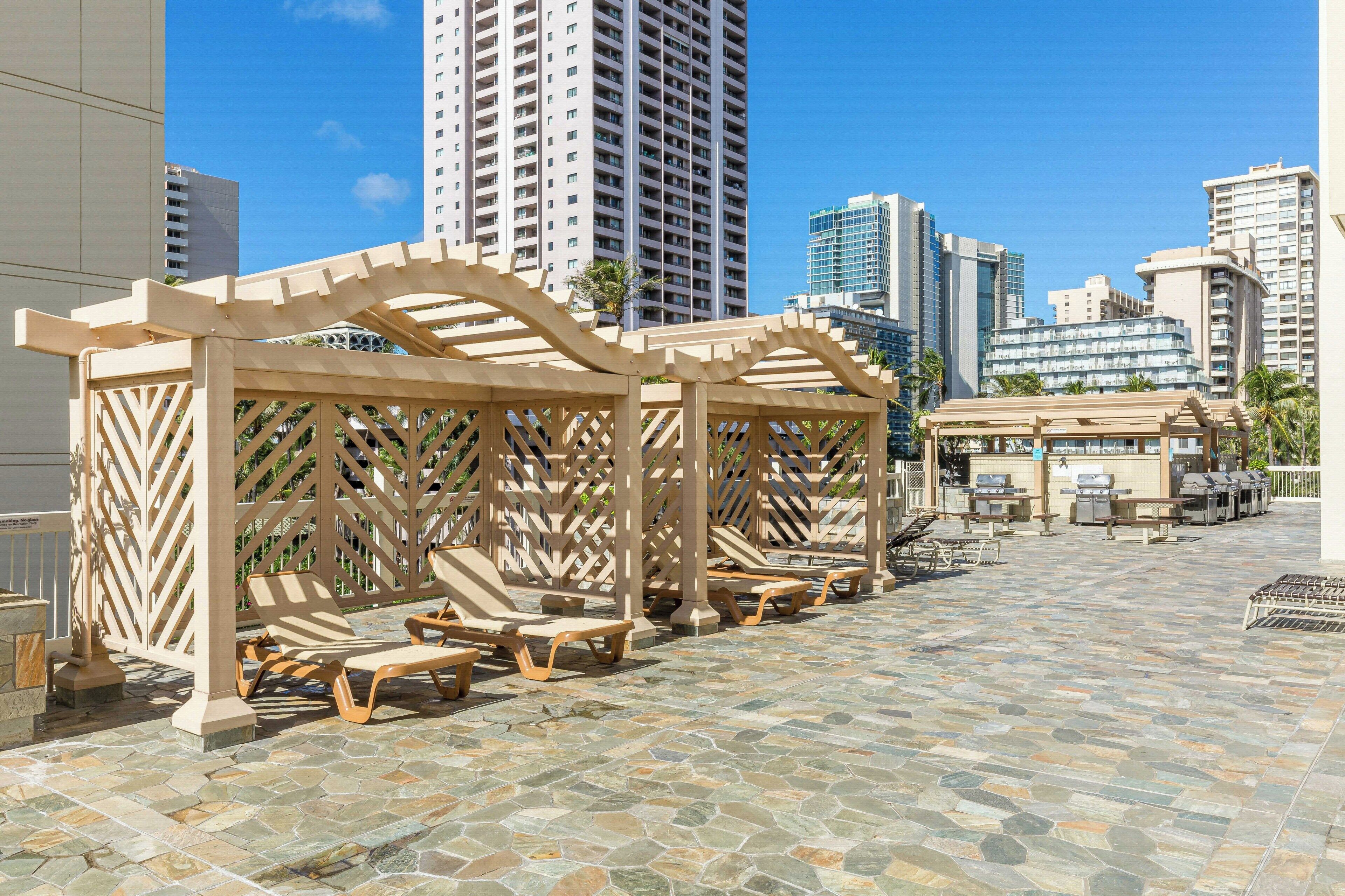 A rooftop patio with lounge chairs, a pergola, and a grill area.