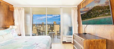 A hotel room with a bed, a desk, a chair, a TV, and a balcony with a city view.