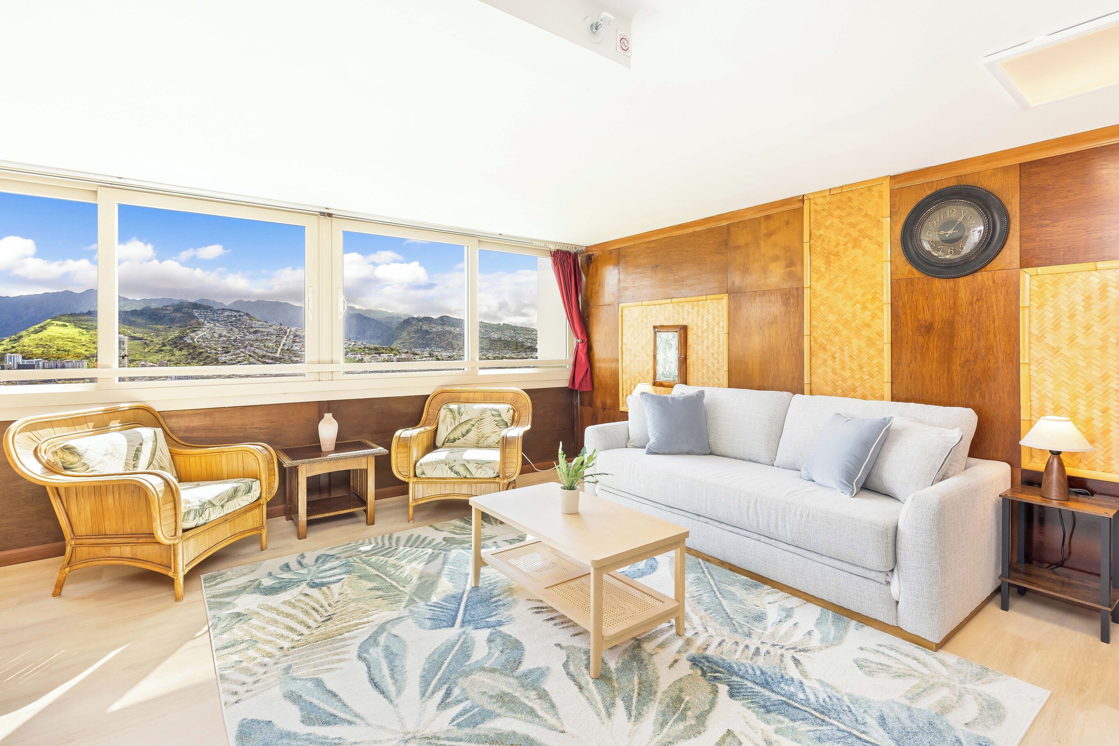 Un salon comprenant un canapé, deux fauteuils, une table basse, une lampe et une vue sur un paysage montagneux grâce à de grandes fenêtres.
