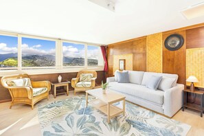 Un salon comprenant un canapé, deux fauteuils, une table basse, une lampe et une vue sur un paysage montagneux grâce à de grandes fenêtres.