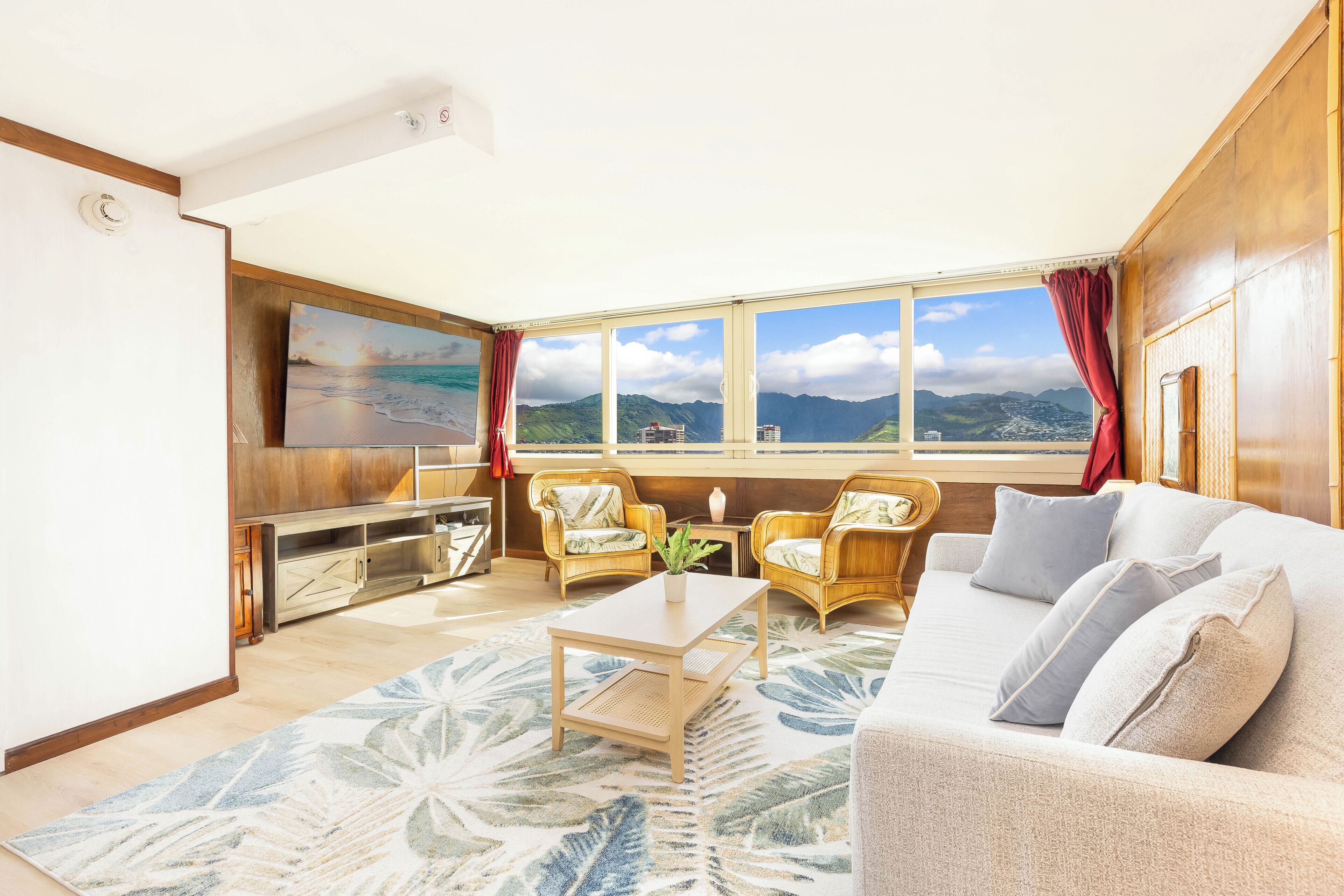 A modern living room with a sofa, chairs, a coffee table, a TV, and a large window with a view of mountains.