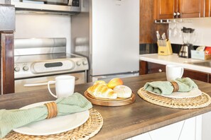 Une cuisine équipée d’une cuisinière, d’un four et d’un plan de travail en bois, agrémentée d’un set de table en fibres tressées, d’une assiette avec une serviette et d’un panier de pain.