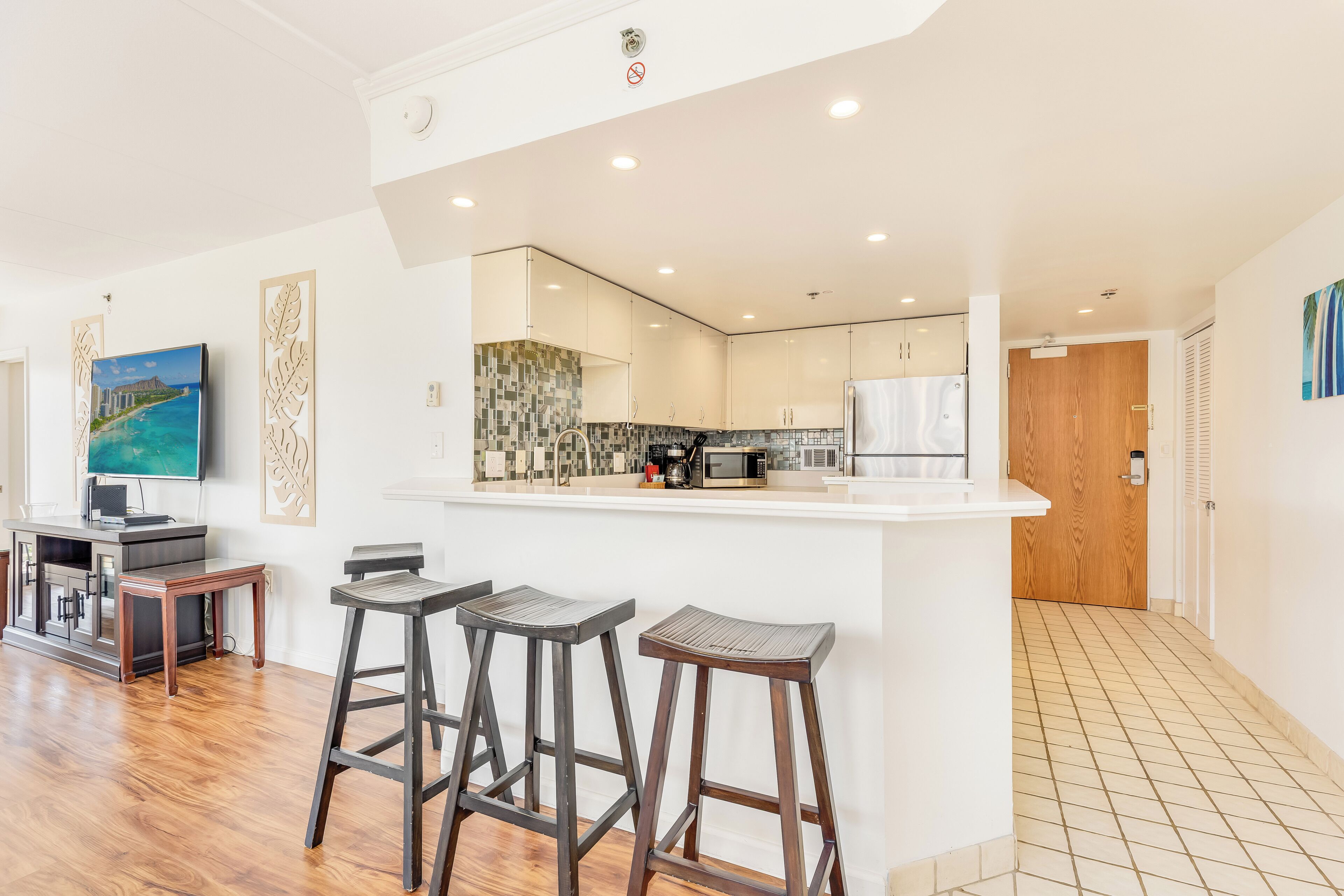 A modern kitchen with a white island, bar stools, and a television.