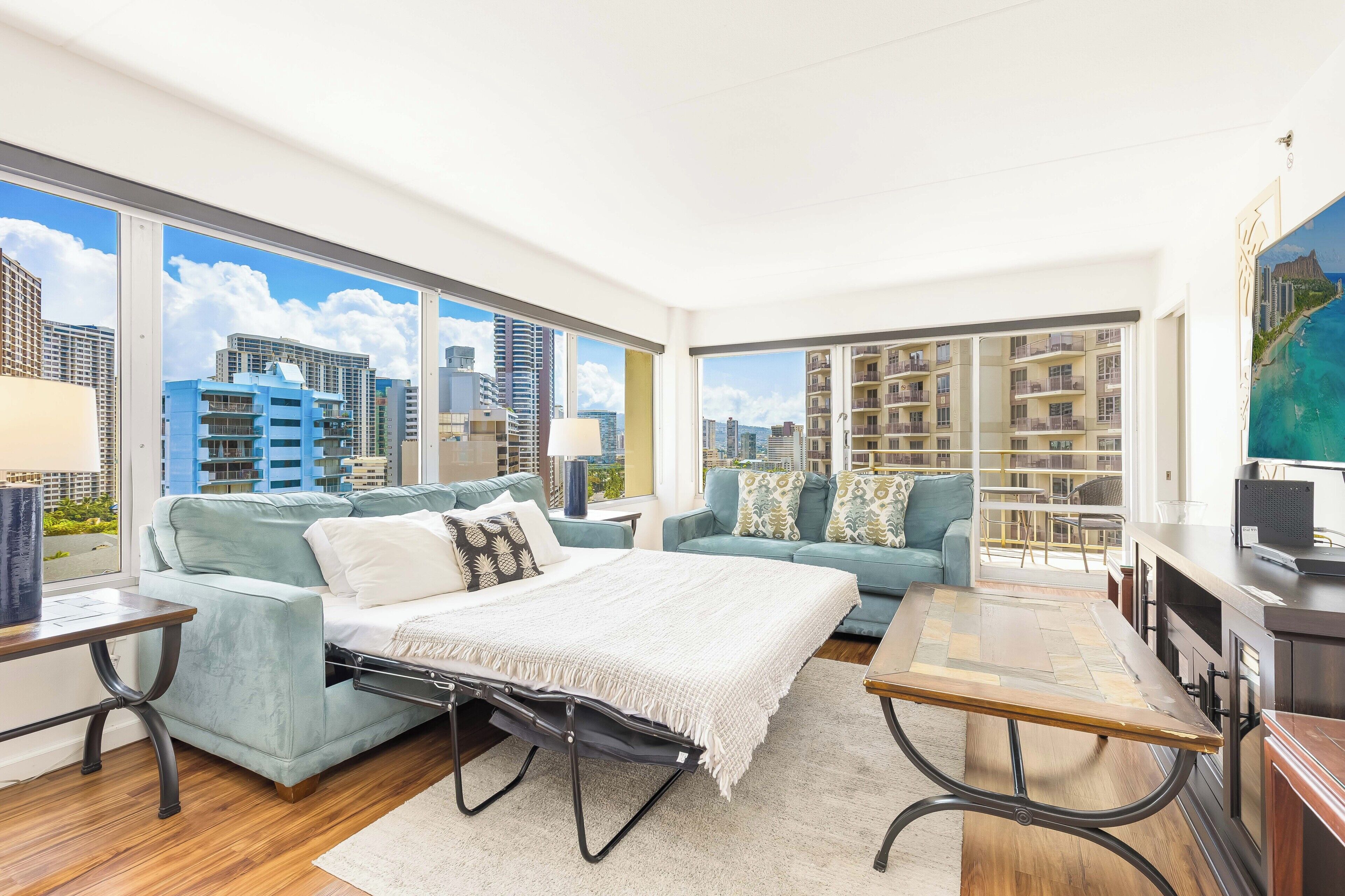 A modern hotel room with a large bed, two sofas, a dining table, and a city view.