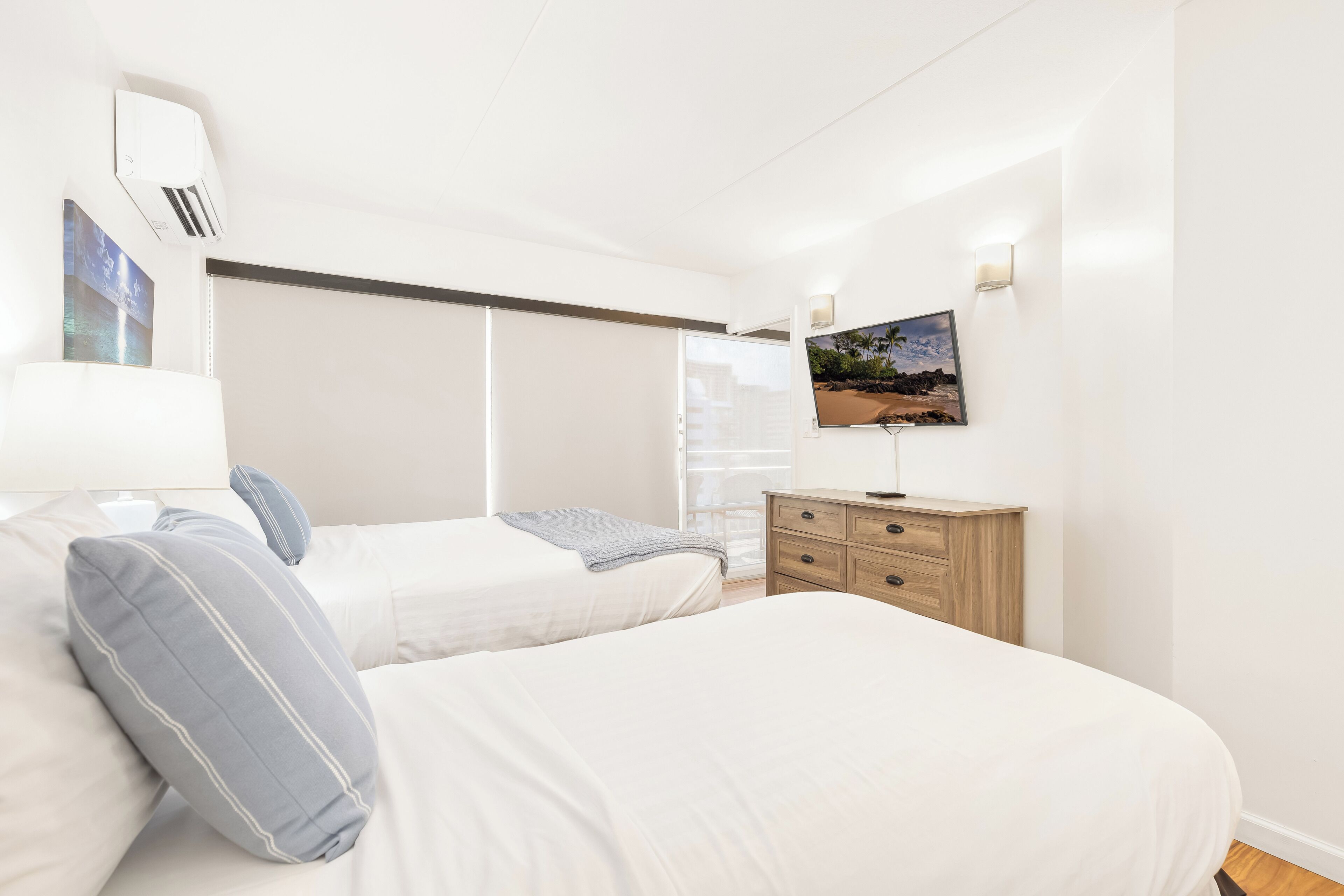 A bedroom with two beds, a TV mounted on the wall, and a wooden dresser.