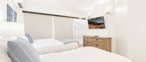A bedroom with two beds, a TV mounted on the wall, and a wooden dresser.