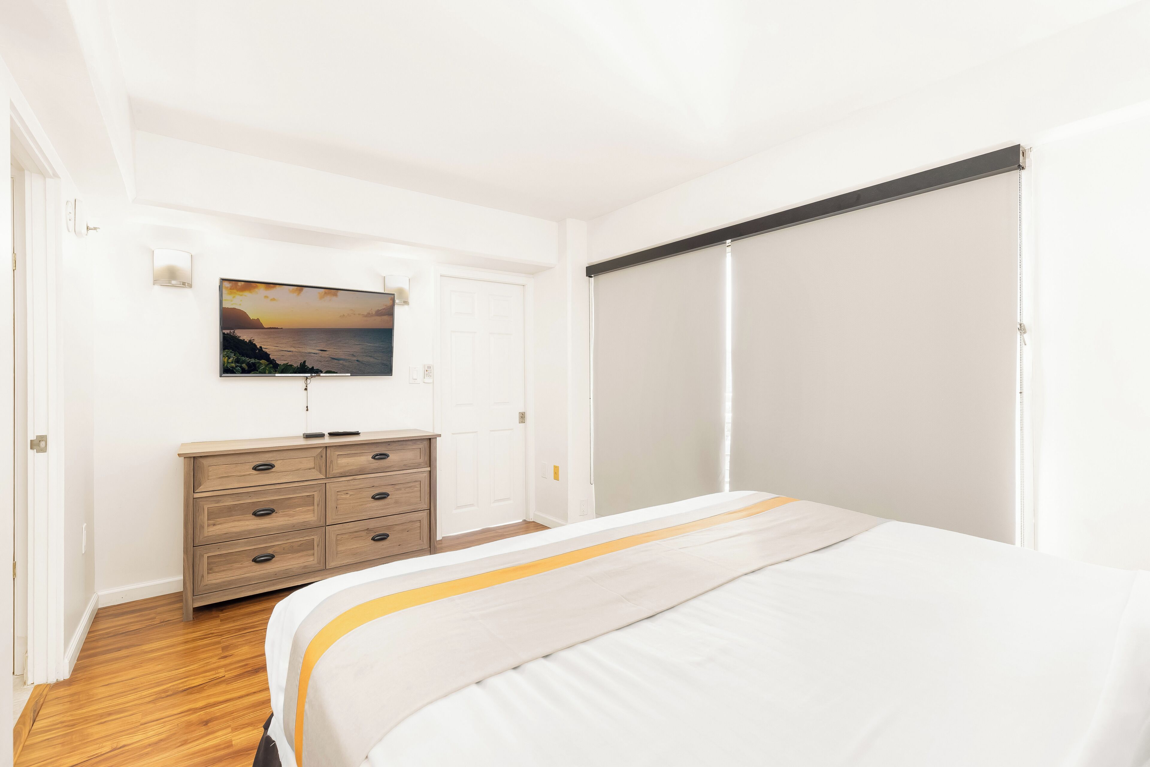 Une chambre à coucher comprenant un lit, une commode, une porte coulissante et un téléviseur fixé au mur.