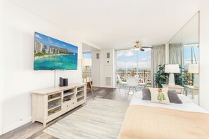 A modern hotel room with a large TV, a bed, a desk, and a balcony with a city view. - Ocean & Marina Views Condo Short Walk to the Beach at the Ilikai Marina (Honolulu)