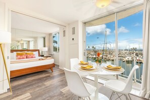 A modern hotel room with a large balcony, a bed, a dining table with chairs, and a view of a marina. - Ocean & Marina Views Condo Short Walk to the Beach at the Ilikai Marina (Honolulu)