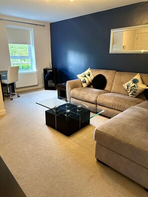 A modern living room with a sofa, a coffee table, and a radiator. - Modern 3-Bedroom Home in Wakefield – Sleeps 5 (Wakefield)