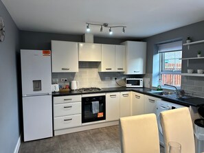 A modern kitchen with white cabinets, a built-in oven, a microwave, and a gas stove. There is a window with a view of the outside, and a sink with a dish rack. - Modern 3-Bedroom Home in Wakefield – Sleeps 5 (Wakefield)