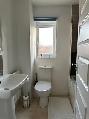 A small bathroom with a toilet, a sink, a window, and a door. - Modern 3-Bedroom Home in Wakefield – Sleeps 5 (Wakefield)