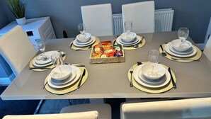 Ein Esstisch, gedeckt für sechs Personen, mit weißen Tellern, goldrandigen Schalen und einer Snack-Korb.