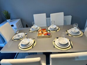 A dining table set for six with white plates, gold-rimmed bowls, and a basket of snacks. - Modern 3-Bedroom Home in Wakefield – Sleeps 5 (Wakefield)