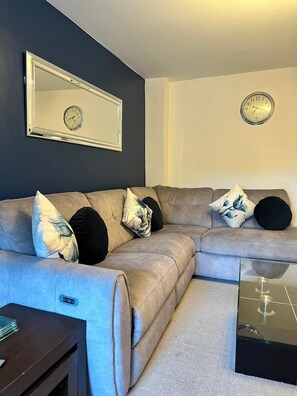 Ein modernes Wohnzimmer mit einem Ecksofa, einem Couchtisch, einer Wanduhr und einem gerahmten Spiegel.