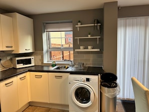 A compact kitchen with a washing machine, a microwave, and a sink. - Modern 3-Bedroom Home in Wakefield – Sleeps 5 (Wakefield)