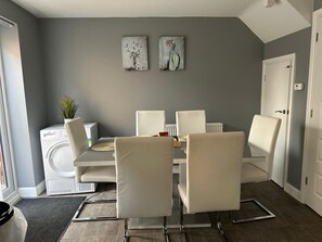 Ein moderner Essbereich mit grauer Wand, zwei gerahmten Kunstwerken, einem weißen Esstisch und sechs Stühlen.