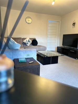 A living room with a sofa, a coffee table, a TV stand, and a glass-top table. - Modern 3-Bedroom Home in Wakefield – Sleeps 5 (Wakefield)