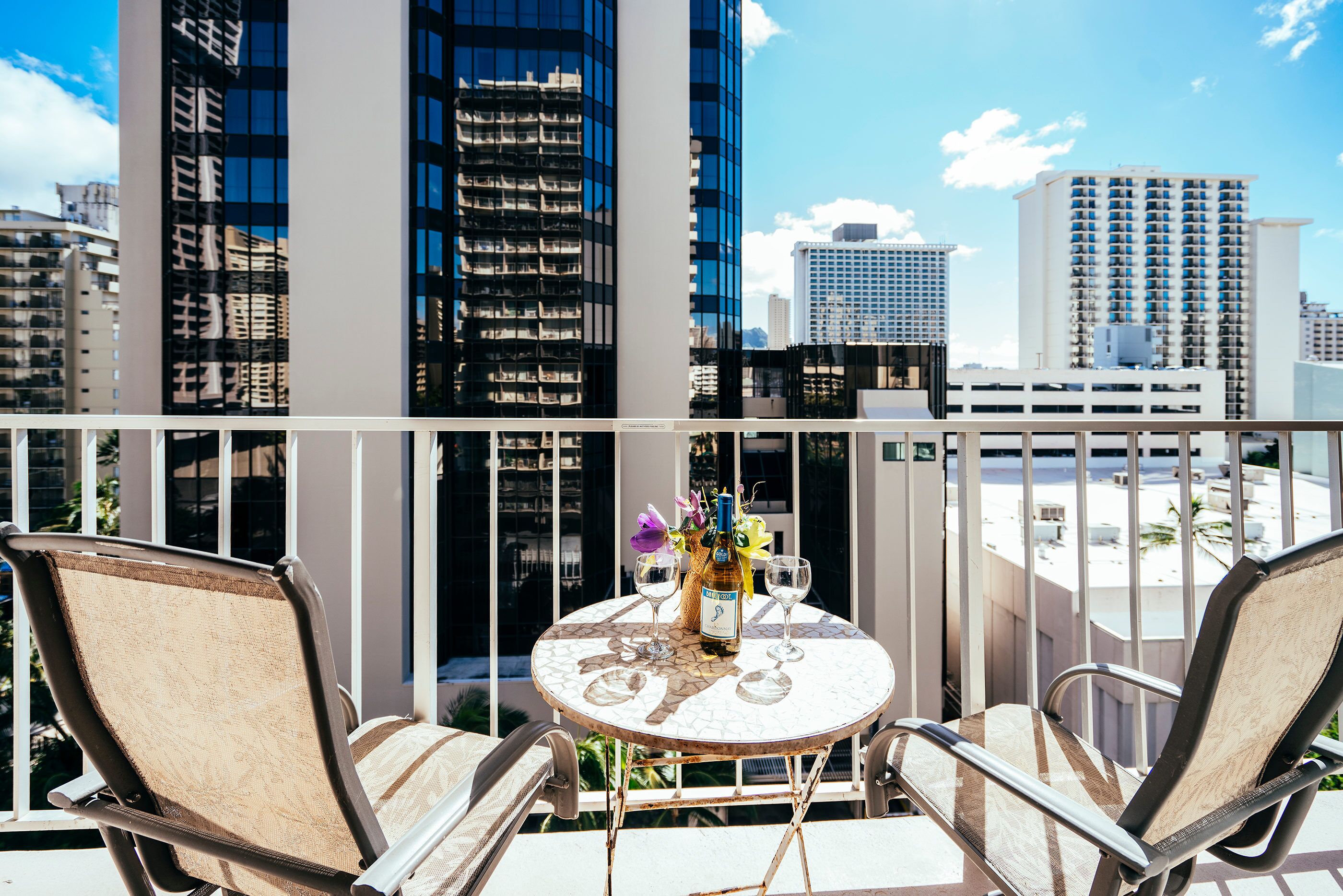 A balcony with two chairs, a table with a bottle and glasses, and a city view.