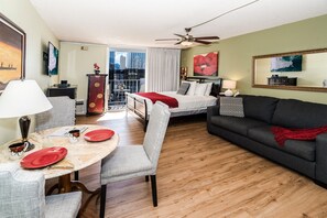 Une chambre d’hôtel comprenant un lit, un canapé, une table à manger avec des chaises, un balcon avec vue sur la ville et un ventilateur de plafond.
