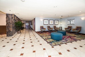 Eine Hotelhalle mit Steinwand, Fliesenboden, Korbstühlen und einem farbenfrohen Teppich.