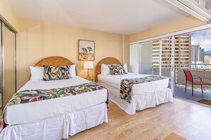 Une chambre d’hôtel avec deux lits, un balcon avec une chaise rouge et une vue sur la ville.