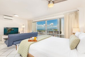 A hotel room with a bed, a sofa, a TV, and a balcony with a view of the sea. - Ocean and Sunset Marina Views at the Ilikai Hotel W/great Building Amenities (Honolulu)