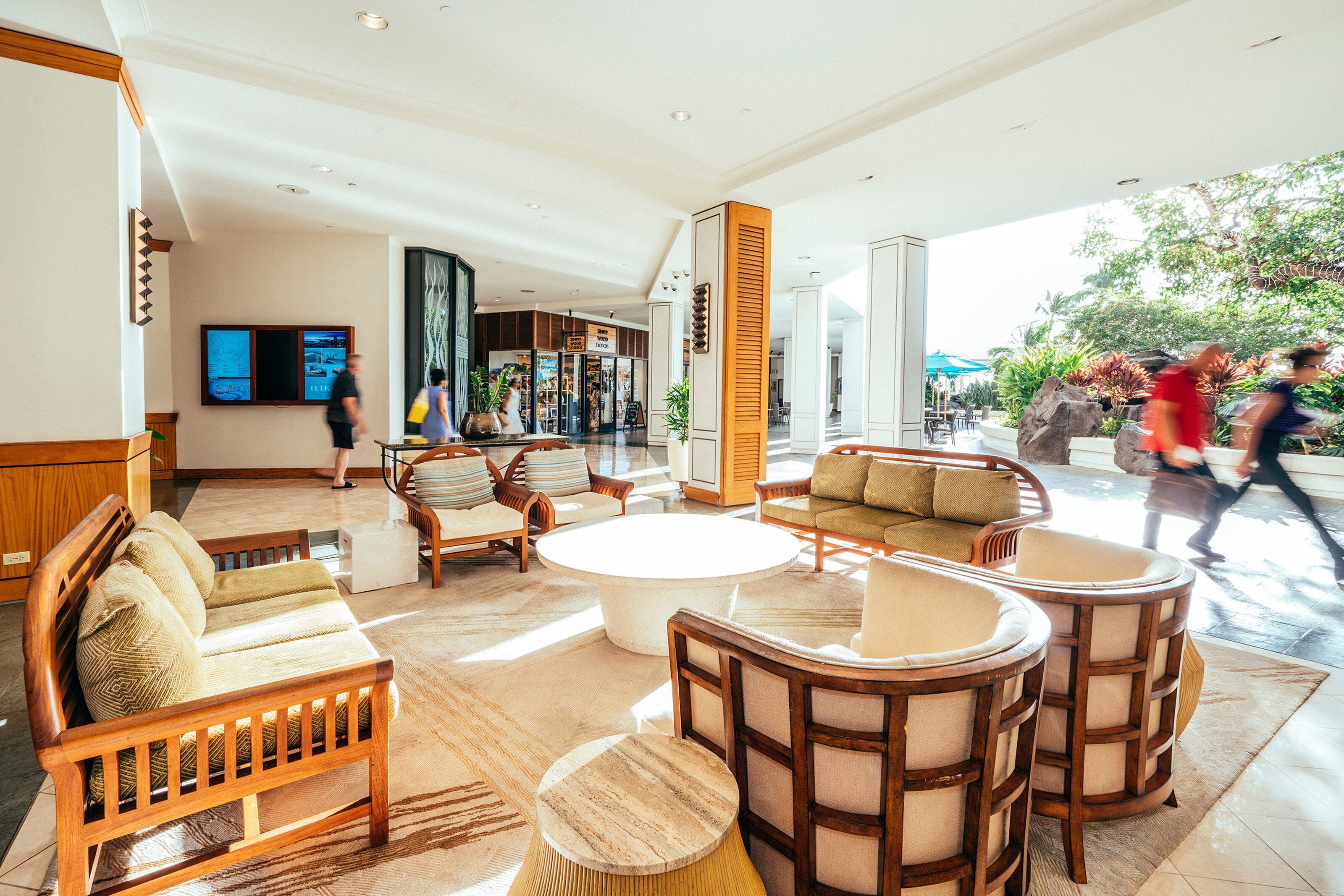 A spacious lobby with a coffee table, sofas, and chairs, a large digital display, and a view of the outside.