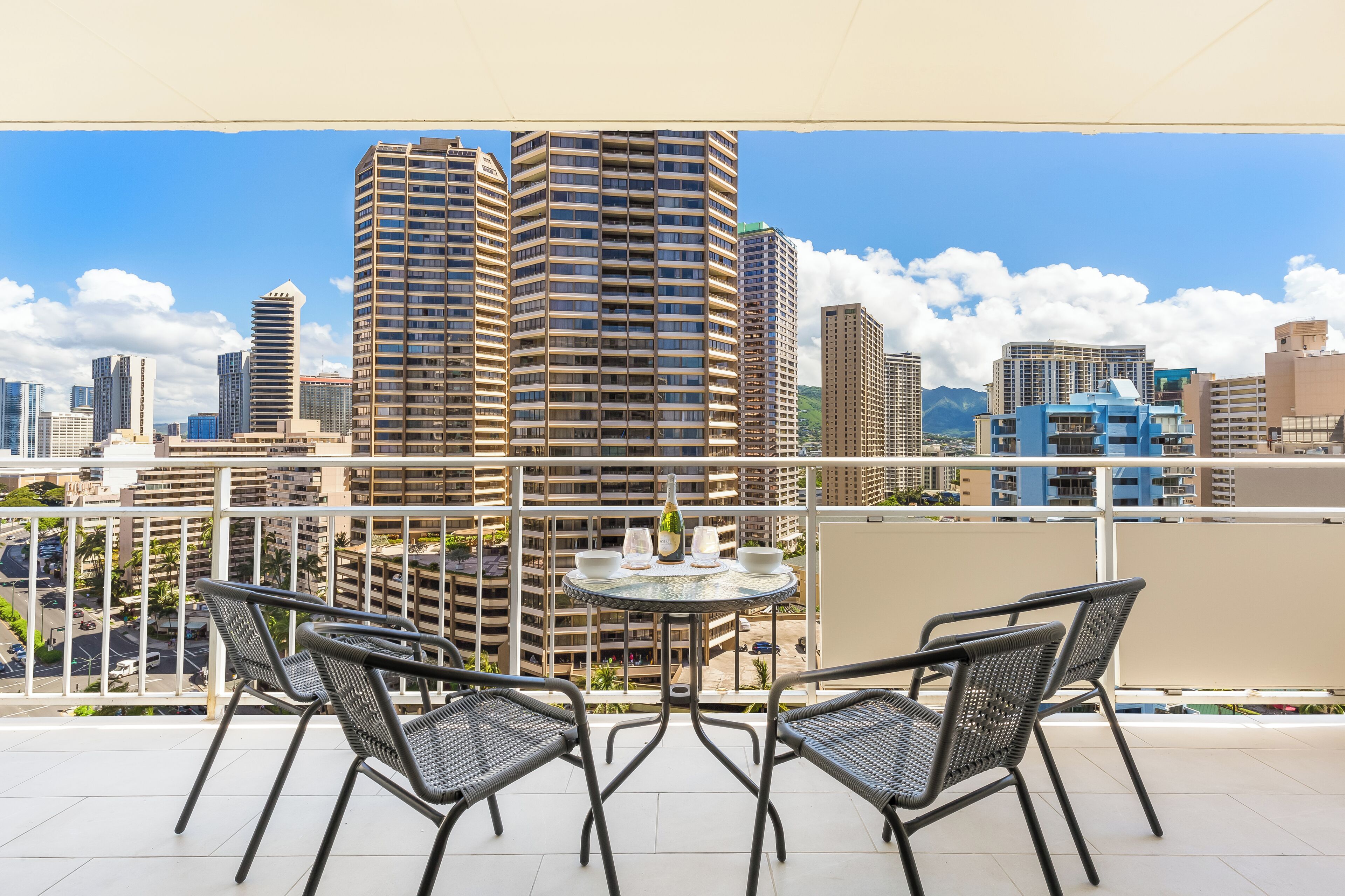 A balcony with two chairs and a table, overlooking a cityscape with tall buildings.