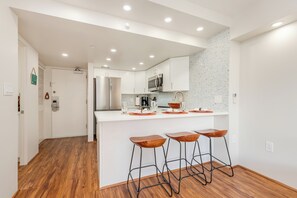 Cozinha moderna com armários brancos, eletrodomésticos de aço inoxidável e uma ilha central com banquetas.