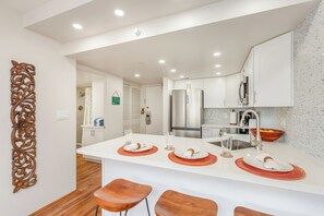 A modern kitchen with white cabinetry, stainless steel appliances, and a central island with bar stools. - Tropical City Escape at Ilikai Hotel by the Beach W/great Building Amenities (Honolulu)