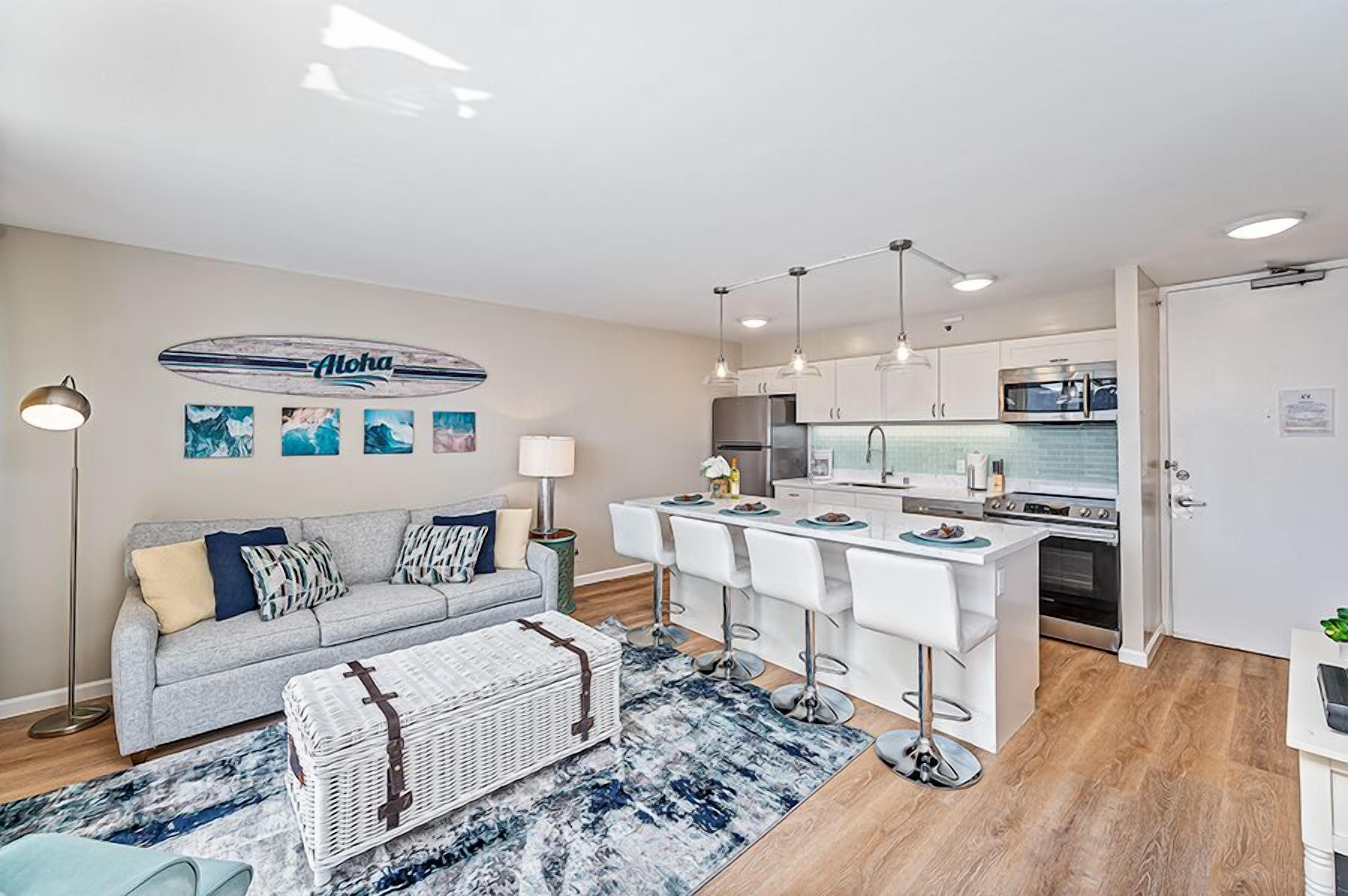 A modern living room with a grey sofa, a coffee table, and a dining area with bar stools.