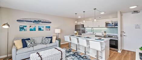 A modern living room with a grey sofa, a coffee table, and a dining area with bar stools.