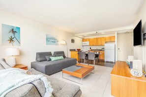 Ein modernes Wohnzimmer mit einem grauen Sofa, einem Holztisch und einer Küche im Hintergrund.