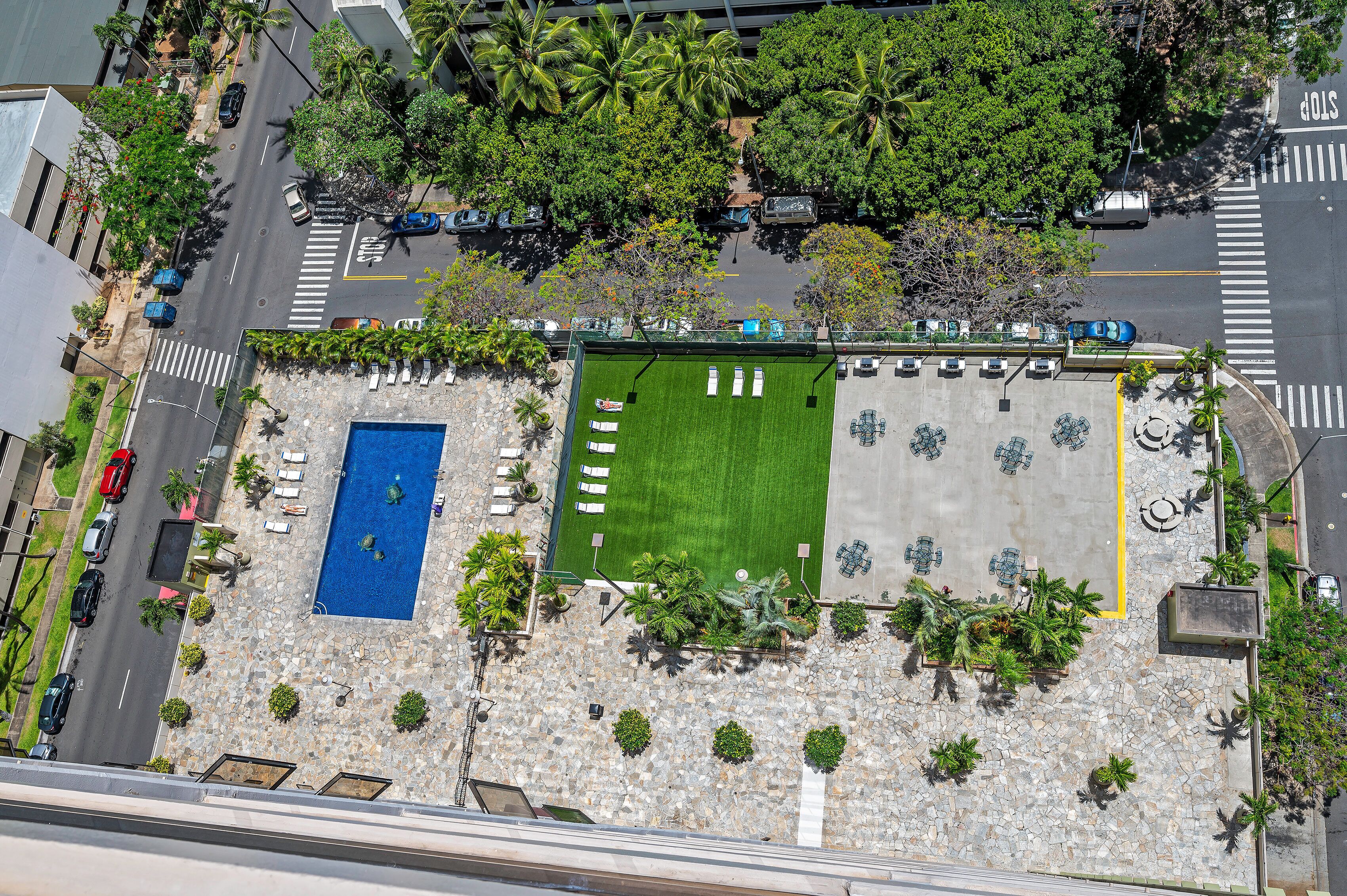 An aerial view of a rooftop with a swimming pool, a green lawn area, and a parking lot.