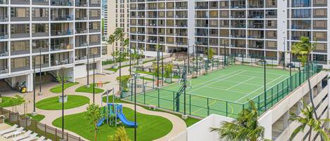 A multi-story residential building with balconies, a tennis court, and a playground.