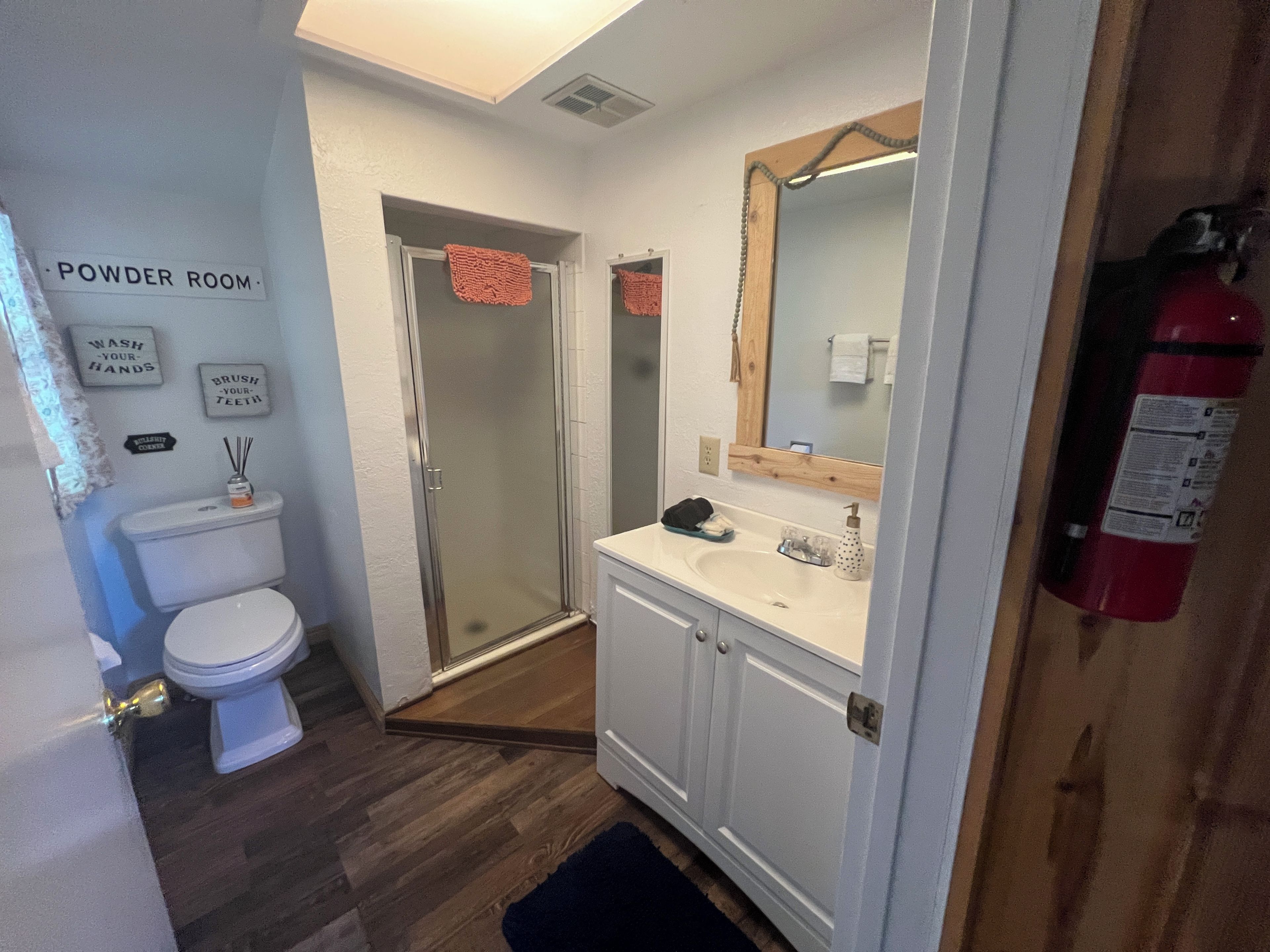 A bathroom with a toilet, shower, and sink. There are signs on the wall and a fire extinguisher mounted on the wall.