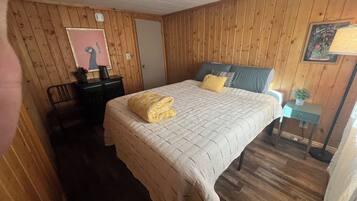 Una stanza con un letto, una scrivania, una sedia, un tavolino con una pianta, e un muro decorato da un quadro e una targa.