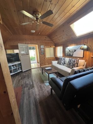 A cabin interior with a ceiling fan, a television, a sofa, and a dining table. - Warm and Cozy 2-bedroom house in fabulous McCall with AC (McCall)