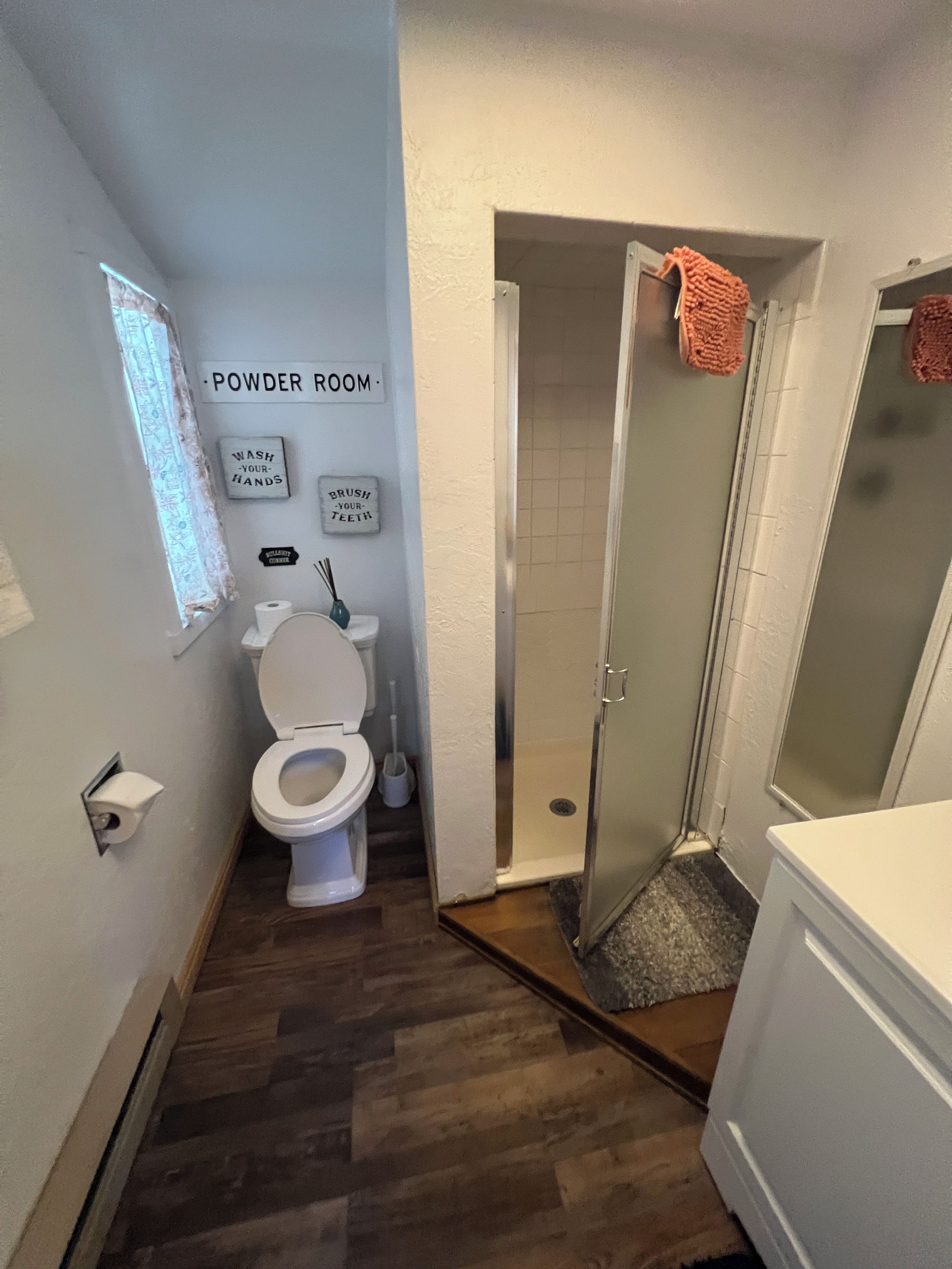 Une salle de bain comprenant des toilettes, une douche et un lavabo. Des panneaux sont affichés sur le mur pour indiquer l’emplacement du lavabo et rappeler de se laver les mains et de se brosser les dents.
