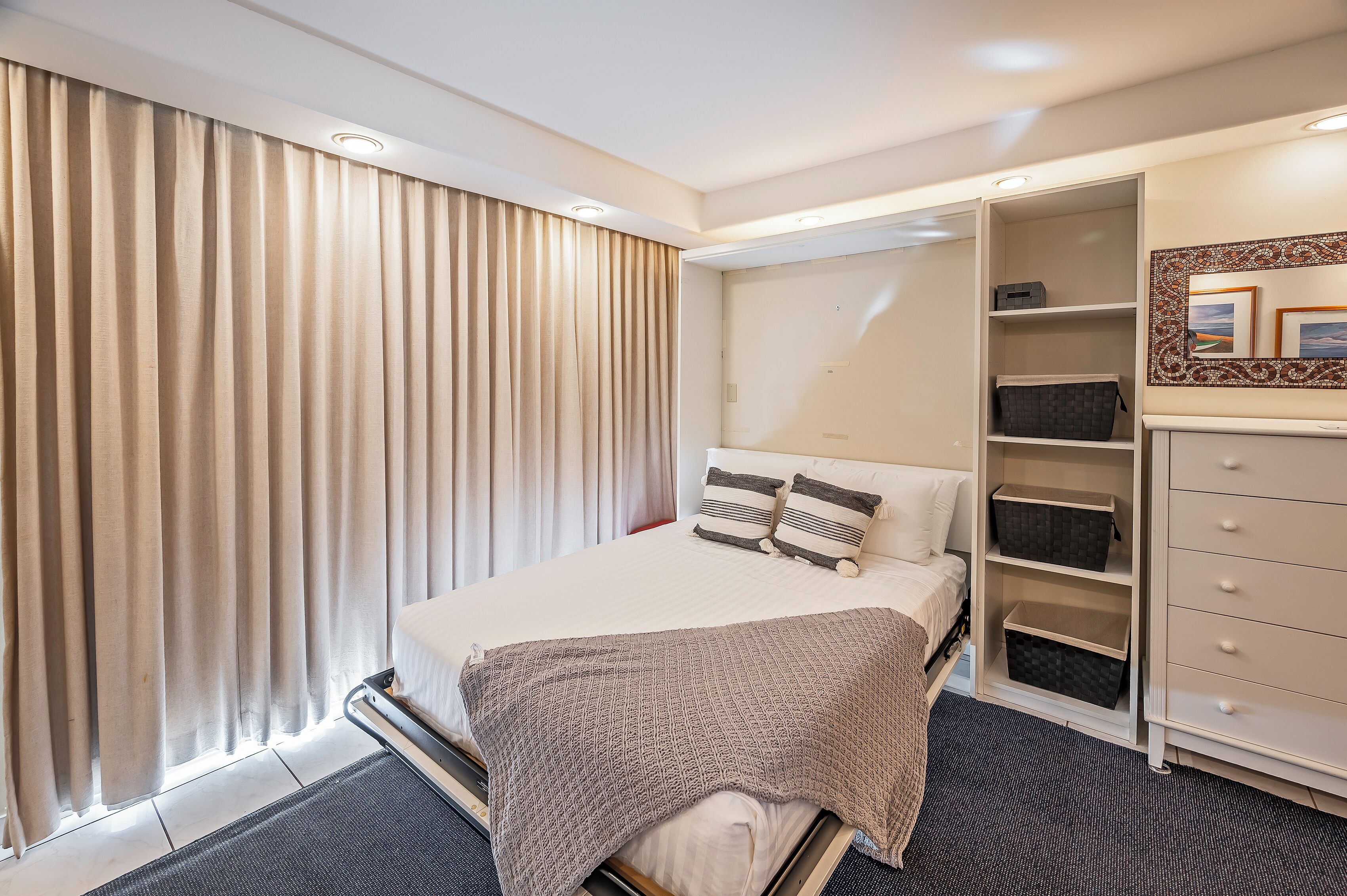 A hotel room with a bed, a wardrobe, and a large window with curtains.