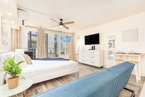 Ein Hotelzimmer mit Bett, Schreibtisch, Fernseher und einem Balkon mit Blick auf Gebäude.