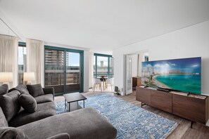 A modern living room with a grey sofa, a coffee table, a large flat-screen TV, and a blue patterned rug. - Panoramic Cityscape Condo at the Waikiki Landmark W/great Building Amenities (Honolulu)