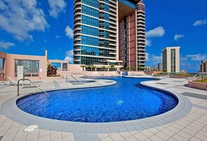 A large outdoor swimming pool with a modern building in the background. - Panoramic Cityscape Condo at the Waikiki Landmark W/great Building Amenities (Honolulu)