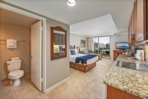 Une chambre d’hôtel avec salle de bain, un lit, un coin cuisine et vue sur la ville.