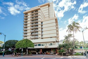A tall, beige multi-story hotel with balconies on each floor, a covered entrance, and palm trees in the vicinity. - Luana at Waikiki Getaway in the Heart of Waikiki (Honolulu)