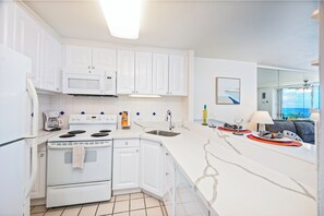 A modern kitchen with white cabinetry, a built-in microwave, a stove, and a large island with a sink. - Ocean-marina Yacht Views Condo Steps to the Beach W/full Kitchen & Free Wifi (Honolulu)